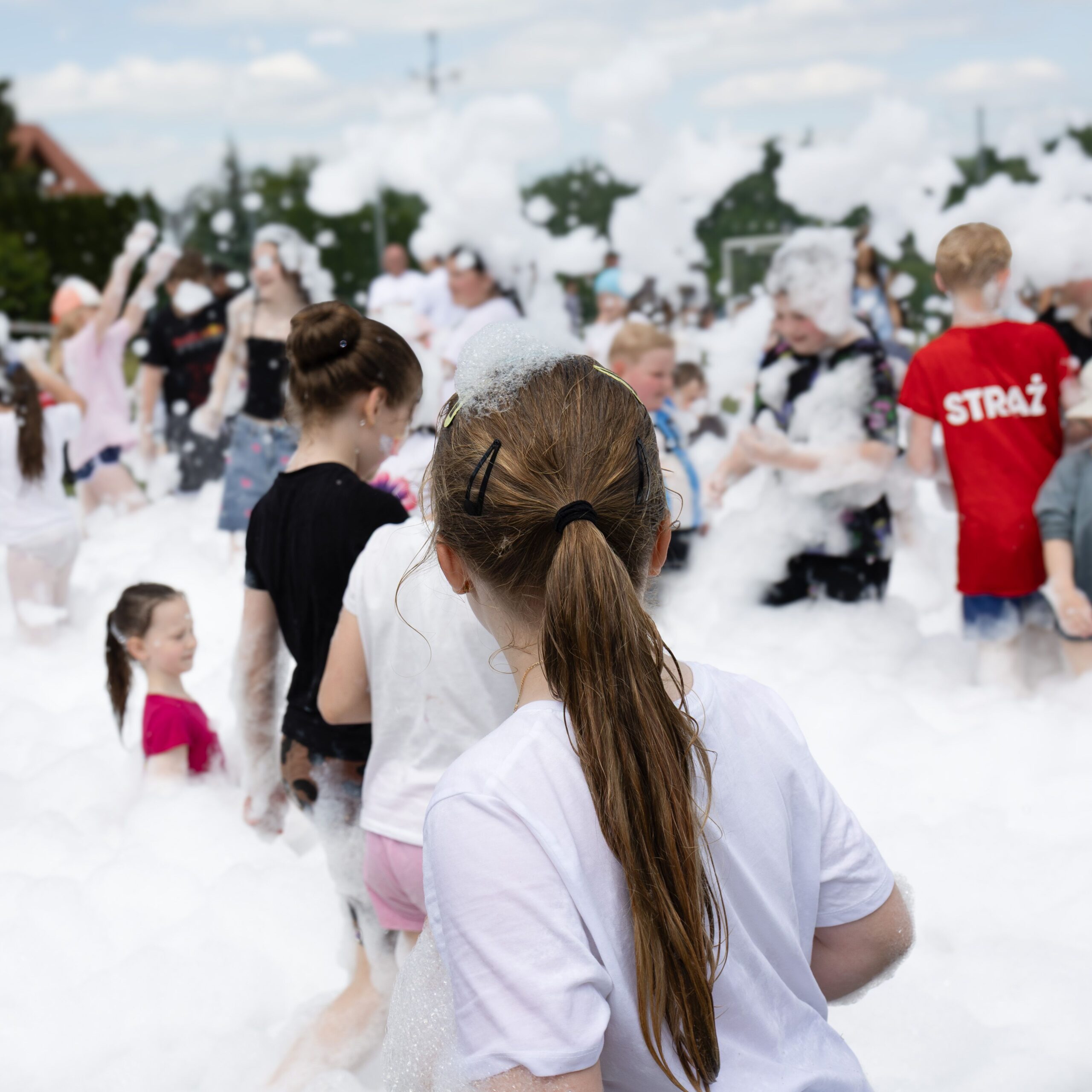 Lively outdoor scene with kids playing in a foam party, having fun under a sunny sky.